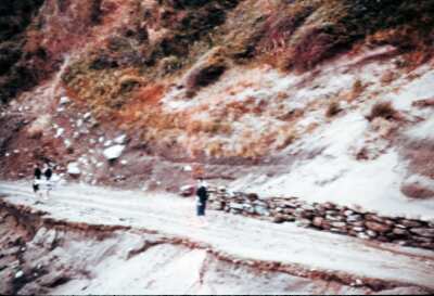 Plano entero de tres mujeres caminando por un camino de tierra en un cerro no identificado