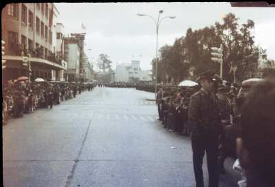 Plano entero de gran cantidad de personas ubicadas a los costados de una calle esperando a que pase un desfile en plaza de armas de Osorno