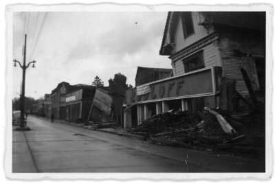plano general de tres casas derrumbadas. En el frontis de una de ellas se encuentra en el suelo y sobre el hay un lienzo colgado. Sobre la vereda se encuentra una ruma de escombros. Las construcciones fueron afectadas por el terremoto del 60' en la ciudad de valdivia