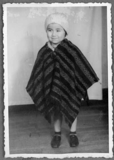 Retrato de Plano General de niña delante de una cortina. La niña tiene puesto un poncho y un gorro