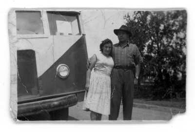 Retrato de un hombre y una mujer al lado de una micro. El hombre viste camisa y sombrero, y la mujer un vestido.