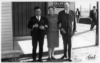 -Retrato de plano entero de Olga Boettcher, posando tomada del brazo de dos hombres. Se encuentran en la entrada de la escuela Nº10 de Trumao --Jorge Alessandri---