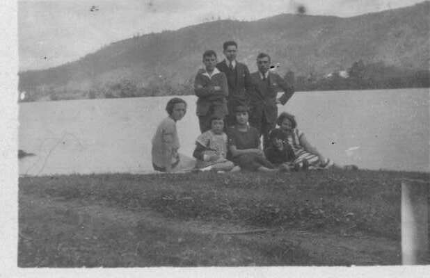 Retrato grupal de plano entero de dos hombres, dos mujeres, tres niñas y un niño posando a orillas de un RÍO no identificado