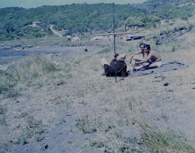 plano general de tres hombres conversando sentados en la arena de una colina ubicada frente a la playa de Hueicolla