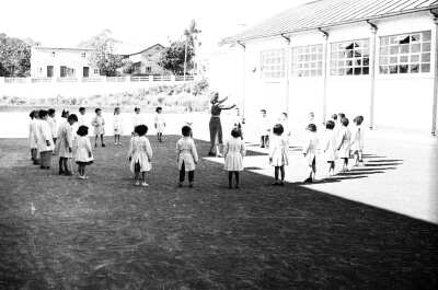 plano general de una Mujer realizando una dinámica en el medio de un círculo compuesto por Niñas y Niños parados usando delantales. La actividad se está llevando a cabo en el patio de la Escuela Nº2 de La Unión