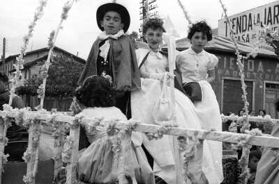 -Plano entero de una Niña y la pareja de reyes de la escuela de Niñas Nº2 mirando hacia la cámara. Se encuentra en el interior de un carro alegórico, el cual avanza por afuera de una tienda llamada --La Jardinera---