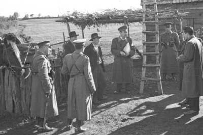 plano general de un grupo de carabineros reunidos en compañía de dos hombres con sombrero y otros dos hombres de abrigo, en el patio de una casa rural, en la cual están recreando un asalto. La casa está ubicada en un territorio no identificado