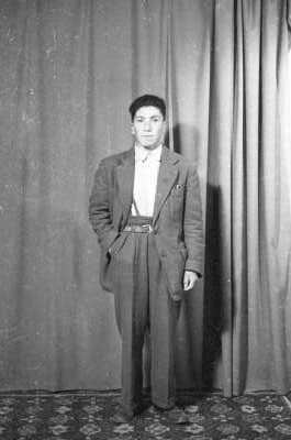 Retrato de estudio de plano entero de un hombre de traje posando de frente con una mano en el bolsillo de su pantalón. Está parado sobre una alfombra
