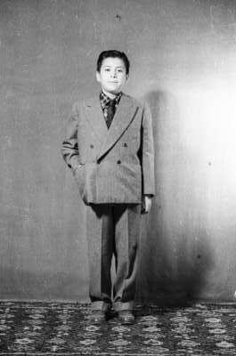 Retrato de estudio de Plano entero de niño con Traje de pie mirando hacia el frente con una mano en el bolsillo