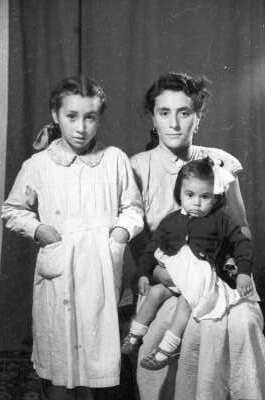 Retrato de estudio de Plano entero de una mujer posando con una niña sobre sus piernas y otra parada junto a ella