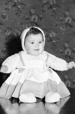 Retrato de estudio de Plano entero de Bebé con Vestido de lana y delantal sentada en una mesa de frente