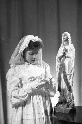 Retrato de estudio de Plano medio de una niña posando con una biblia en la mano. Está usando la vestimenta típica utilizada para las primeras comuniones