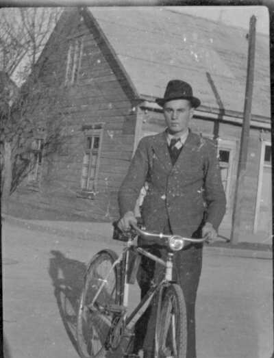 Plano medio largo de un hombre joven posando de pie junto a una bicicleta en una calle pavimentada